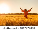 African woman in traditional clothes standing arms raised in field of barley or wheat crops at sunset or sunrise