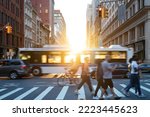 People, cars, bikes and buses traveling through a busy intersection on 5th Avenue and 23rd Street in New York City with sunlight shining in the background