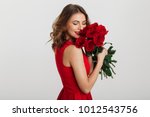 Portrait of an attractive young woman dressed in red dress holding bouquet of roses isolated over white background