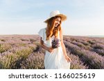 Cheerful young girl in straw hat holding lavender bouquet at the field