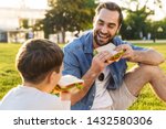 Happy young father having a picnic with his little son at the park, eating sandwiches