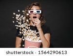 Image of a concentrated cute young woman in 3d glasses isolated over dark grey wall background eat popcorn watch cinema.