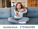 Photo of excited nice girl smiling and playing video game with joystick while sitting on couch at home