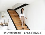 Confident smiling young asian business woman walking down the staircase in the kitchen at home