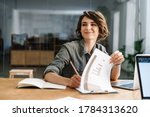 Image of smiling beautiful woman writing down notes while sitting at table in office