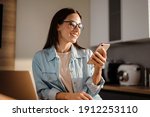 Happy charming woman using smartphone while working with laptop at home