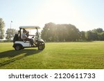Small photo of Side view of golfers riding golf cart on green lawn of golf field at warm sunny day. Concept of entertainment, recreation, leisure and hobby outdoors. Idea of frienship. Young caucasian male friends