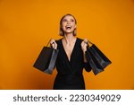 Portrait of young excited woman holding shopping bags and looking up standing isolated over orange background