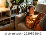 Brunette young woman listening music and using cellphone while resting on couch at home
