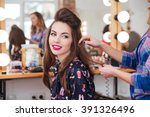 Female hairdresser standing and making hairstyle to cute lovely young woman in beauty salon