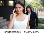 Beautiful young woman talking on mobile phone and being stalked by man criminal on the street