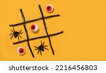 Small photo of Game tic-tac-toe from spiders and eyes on orange background. Halloween party