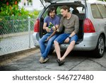 Small photo of Two young men drink beer from bottles. They have conveniently settled down in an open luggage carrier of the car. Friends derive pleasure from beer and communication.