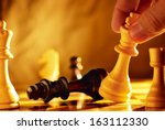 Small photo of Close up view of the hand of a man going for checkmate in a game of chess using his king to knock over the opposing piece with dramatic sepia toned lighting and copyspace