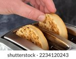 Small photo of Man taking a toasted crumpet from an electric toaster appliance. On a dark stone background
