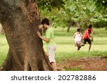 young boys and girls playing hide and seek in park, with kid counting leaning on tree
