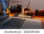 Photographer drawing and retouching image on laptop computer, using a digital tablet and stylus pen. Closeup of man's hand with dslr camera in background. Copy space in foreground