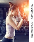 Small photo of Young slim woman doing pushdown on cable machine in gym in sunset beams. Athletic girl training triceps in fitness center