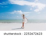 Happy traveller woman in white dress and hat enjoys her tropical beach vacation