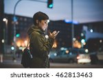 Half length of young handsome caucasian brown straight hair woman holding a smartphone looking down the screen in city night, face illuminated by screen light - technology, communication concept