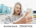 Young beautiful caucasian purple grey hair woman outdoor in the city outdoor in city back light taking selfie with smart phone hand hold doing grimace - vanity, social network, sharing concept
