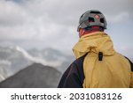 Rear view of sporty hiker man looking snowy landscape from mountain peak. Back view of man with backpack standing with copy space. Climber thinking while looking at a snowy winter landscape.