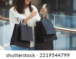 No face portrait of beautiful plus size woman happy with many purchases in paper bags bought on sale in a shopping mall and writing message in smartphone