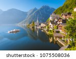 Classic postcard view of famous Hallstatt lakeside town with traditional ship in beautiful morning light at sunrise in summer, Salzkammergut, Austria