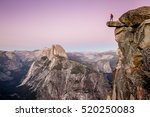 A male hiker standing on an overhanging rock at Glacier Point enjoying the breathtaking view towards famous Half Dome in beautiful twilight after sunset in summer, Yosemite National Park, California