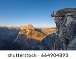 A fearless hiker is standing on an overhanging rock enjoying the view towards famous Half Dome at Glacier Point overlook in beautiful evening sunset twilight, Yosemite National Park, California, USA