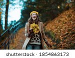 Hello september. happy trendy female in brown coat and yellow hat with autumn yellow leaves enjoying promenade outside in the city park in autumn.