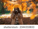 Hello september. elegant middle aged woman in beige coat and orange hat with napkin blowing nose outside on the city park in autumn.