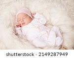 Small photo of Newborn Baby Girl sleeping over Fluffy White Blanket. Adorable One Month Child in Pink Bodysuit dreaming over Beige Furry Carpet. Cute New Born Kid relax
