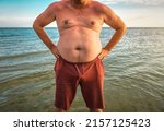 Small photo of Fat stomach male torso on the beach at sunset, overweight theme