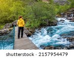Woman in yellow jacket standing on a suspension bridge over mountain river in Norway