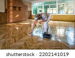 Lacquering parquet floors. Worker uses a roller to coating floors. Varnishing lacquering parquet floor by paint roller - second layer. Home renovation parquet