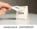 a woman's hand turns over a calendar sheet. year change from 2023 to 2024