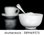Bowl of sugar with spoon.  Coffee cup behind, over black.  Selective focus.