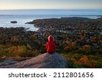 A young woman looks out at the ocean during fall or autumn at Camden Hills State Park in Camden, Maine, USA.