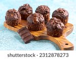 Chocolate muffins with zucchini and chocolate glaze are served on a wooden serving board with a piece of chocolate, selective focus.