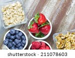Healthy snack foods with small bowls of raspberries, blueberries, strawberries, cashews and walnuts