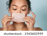 Small photo of Skin care. Woman holding facial oil blotting paper portrait. Closeup of beautiful asian girl model with natural face makeup looking at oil absorbing tissue, beauty product.