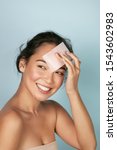 Small photo of Face skin care. Smiling woman using facial oil blotting paper portrait. Closeup of beautiful happy asian girl model with natural makeup using oil absorbing sheets, beauty product at studio