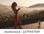 Woman enjoys a peaceful sunrise retreat with a cup of coffee, overlooking stunning views in Bali. Travel and relaxation concepts.