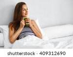 Beautiful Happy Young Woman Drinking Cup Of Coffee Or Tea While Lying In Bed After Waking Up In Morning. Closeup Portrait Of Smiling Girl Enjoying Her Drink While Relaxing At Home.