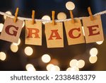The word GRACE printed on clothespin clipped cards in front of defocused glowing lights.