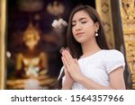 Small photo of Religious Asian buddhist woman praying. Female buddhist disciple meditating, chanting mantra with prayer hand to the statue of lord Buddha in temple hall; concept of asian faith, belief, spirituality