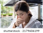 Small photo of Unwell woman wearing raincoat feeling sick, catching cold with runny nose, nasal congestion and fever during rain fall in rainy monsoon season