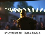 Rock musician with a guitar and a hat on a stage on blurred background of street concert audience