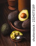 Small photo of Avocado in a clay plate against a dark and moody wooden backdrop. This trendy composition creates a visually appealing contrast. Scraped avocado with half a spoon. Healthy Eating, Dark Moody style.
